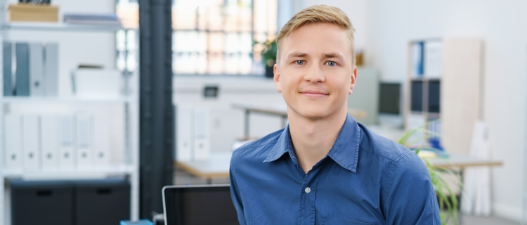 Das Bild zeigt einen jungen Mann an einem Schreibtisch.